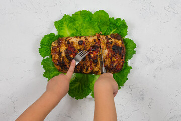 Children's hands are cutting with a knife and holding with a fork a large piece of chopped pork, cooked in the oven, baked in the oven, on green lettuce leaves, close-up.