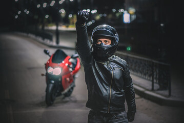 Wall Mural - Motor biker is standing among the night road with raised up fist.