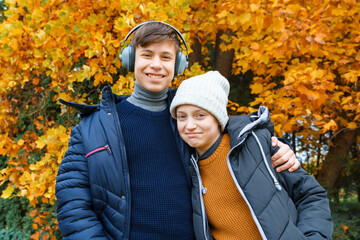 Wall Mural - portrait of a teenager boy and girl listening to music by headphones, relaxing in autumn city park, bright yellow maple leaves as background