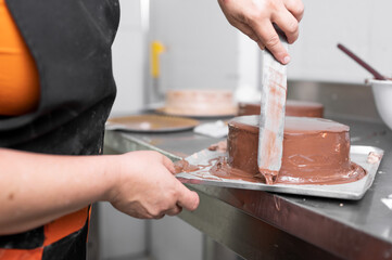 Wall Mural - Woman pastry chef finishing chocolate cake with icing, final stage of cooking. The process of making the chocolate cake. High quality photo