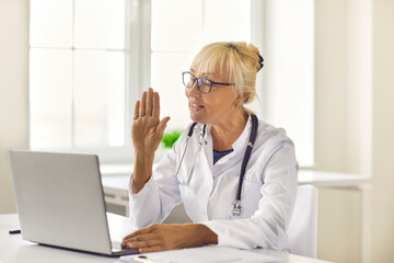 Side view friendly senior female doctor greets the patient and conducts an online consultation.