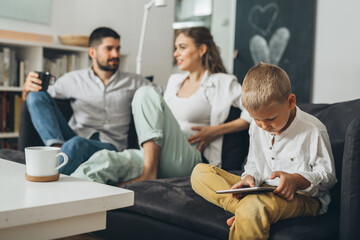 Canvas Print - boy using tablet computer at home, mother and father in blurred background