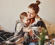 © JenkoAtaman - happy family mother and loving son hug and laugh wrapped in a warm blanket on a cozy winter evening at home .