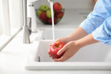 Wall Mural - Woman washing fresh red apple in kitchen sink, closeup