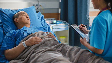 Hospital Ward: Friendly Chinese Head Nurse Fills Medical History Form, Talks to Male Patient Recovering in Bed. Beautiful Professional Nurse Helps Handsome Man Getting Better after Surgery.