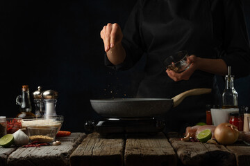 Wall Mural - Professional chef pours hot spices into pan with chicken fillet. Backstage of cooking traditional Indian chicken curry on dark blue background. Frozen motion. Concept cooking process. Frozen motion.