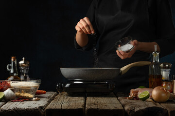 Wall Mural - Professional chef salts chicken fillet in pan. Backstage of cooking traditional Indian chicken curry on dark blue background. Frozen motion. Concept cooking process. Frozen motion.