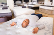 © JackF - Smiling adult hispanic man lying on bed in furniture store, enjoying convenience of modern orthopedic mattress .