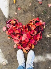 Low Section Of Person Standing By Heart Shape Fallen Dry Leaves During Autumn