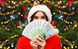 © Syda Productions - winter holidays and finance concept - happy smiling young woman in santa helper hat holding euro money banknotes over christmas tree lights on background