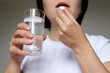 © Oleg - Woman in white top taking pill holding a glass of water. Concept of medication or vitamins