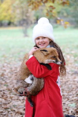 Girl holding fox in her arms in autumn park