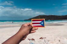 Cropped Hand Holding Flag At Beach Against Cloudy Sky