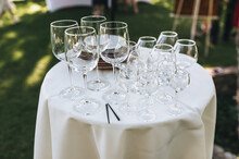 Glass Goblets And Plates Stand On A Round White Table Covered With A Tablecloth As Decorations For A Banquet Or Buffet Table.