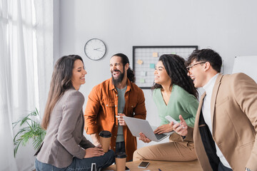 Wall Mural - Cheerful hispanic office workers laughing, while looking at colleague during break at workplace