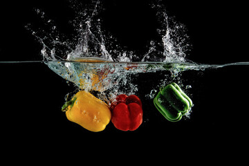 close up view of color pepper vegetable falling into water isolated on black background