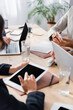 © LIGHTFIELD STUDIOS - Cropped view of businesswoman using smartphone near contract and colleagues using devices on blurred foreground