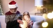 © VAKSMANV - Close up portrait of joyful Caucasian grandpa giving xmas present to cute little girl grandchild while sitting at cozy decorated home near glowing christmas tree. New Year concept. Gifts and presents