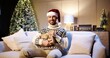 © VAKSMANV - Caucasian cheerful young handsome man in good mood smiling with wrapped gift sitting at decorated house near christmas tree with twinkle lights on Xmas Eve. New Year concept. December holidays