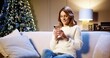 © VAKSMANV - Joyful Caucasian beautiful woman in good mood sitting in cozy room near glowing xmas tree typing on smartphone with happy face. Happy New Year. Merry Christmas concept. Winter holidays