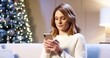 © VAKSMANV - Close up portrait of Caucasian cheerful beautiful woman with surprised face sitting in cozy room near glowing xmas tree typing on smartphone. Happy New Year. Merry Christmas. Winter holidays