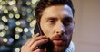 © VAKSMANV - Close up of happy handsome young man speaking on smartphone on Christmas eve sending congratulation. Caucasian joyful male speaking on mobile phone. Winter holidays. Xmas spirit concept