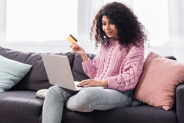 happy young woman holding credit card and using laptop at home