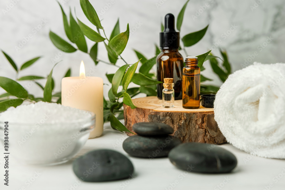 beauty treatment items for spa procedures on white wooden table with green plant. massage stones, essential oils and sea salt with burning candle - obrazy, fototapety, plakaty 