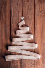 Christmas tree made of linen ribbon on a wooden background. The top of the tree is decorated with a snowflake. The concept of a brutal Christmas. zero waste