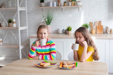 Portrait of two teenage beautiful smiling hipster girls in fashionable clothes. carefree children posing against the backdrop of the kitchen. Positive models have fun with sweets.