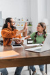 © LIGHTFIELD STUDIOS - Happy hispanic father giving high five to daughter, while sitting at table with devices in kitchen on blurred foreground