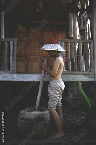 Plakat Asian young farmer pound using traditional mashing tools. Traditional activity in village concept.