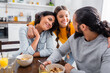 © LIGHTFIELD STUDIOS - Smiling hispanic girl embracing parents near bowls of cereals on blurred foreground