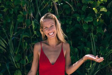 Cheerful young woman in summer outfit standing against tropical plants