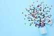 Colorful confetti and box on light blue background, top view. Space for text