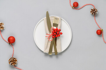 Festive table setting with white plate, golden cutlery and xmas decorations on light gray tabletop. Christmas table setting. Flat lay, top view. Minimal style