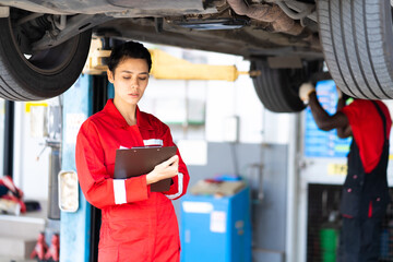 Empowering caucasian waman mechanic wearing red uniform working Under a Vehicle in a Car Service station..Expertise mechanic working in automobile repair garage.