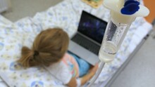 Young Girl On A Drip With Peripheral Venous Catheter Using Laptop In Hospital
