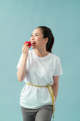 Wall Mural - Beautiful sporty woman using tape measure eating apple fruit over blue background