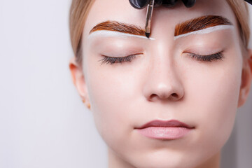 Beautiful young girl tweezing her brows in a beauty salon. Beauty Concept. Cosmetologist plucks client eyebrows by thread. Eyebrow correction, threading. Permanent Makeup. Microblading brow. Close up.