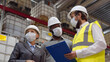 © TommyStockProject - Diverse warehouse inspectors wearing safety mask discussing distribution plan on clipboard