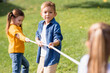 © LIGHTFIELD STUDIOS - Boy holding rope while playing tug of war with friends on blurred foreground in park