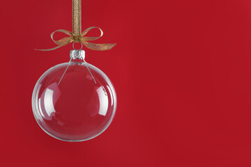 Poster - Transparent glass Christmas ball with golden ribbon and bow against red background. Space for text