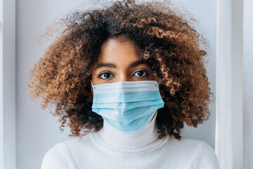 Wall Mural - Portrait of an African-American girl in a protective medical mask close-up looks at the camera, protection from the coronavirus pandemic