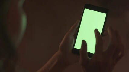 Poster - Close-up of a woman tapping on a green phone screen. Stock. Woman runs fingers over green screen of phone in fascination. Woman taps green screen of phone on background of dark room