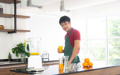 Portrait smart and handsome Asian man preparing healthy meal and fresh organic orange juice in the loft style kitchen.