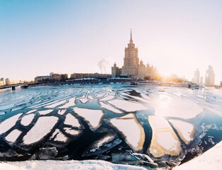 MOSCOW, RUSSIA - Radisson Royal Hotel (former hotel Ukraine) winter city skyline panorama with sunset sky, floating ice on the river.  Sunny winter city landscape. Spring is coming, ice melting 