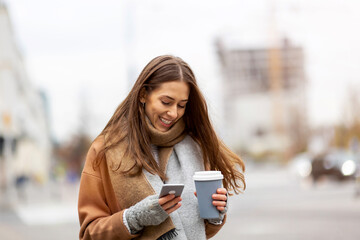 Wall Mural - smiling young woman with smart phone and coffee cup outdoors at urban setting