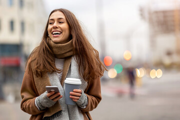 Wall Mural - smiling young woman with smart phone and coffee cup outdoors at urban setting