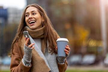 Wall Mural - smiling young woman with smart phone and coffee cup outdoors at urban setting